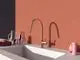 Küchenarmatur in Rosé mit hohem Auslauf vor einem orangefarbenen Wandhintergrund. Neben der Armatur stehen ein Glas Krug und verschiedene Küchenutensilien. Marke: Ideal Standard.